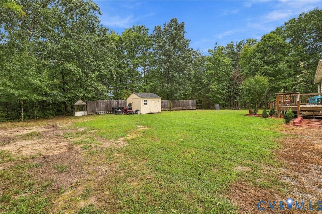 133 Ford Road, Bumpass, VA 23024 Expansive backyard featuring a manicured lawn, established trees, a wood privacy fence, and a detached storage shed