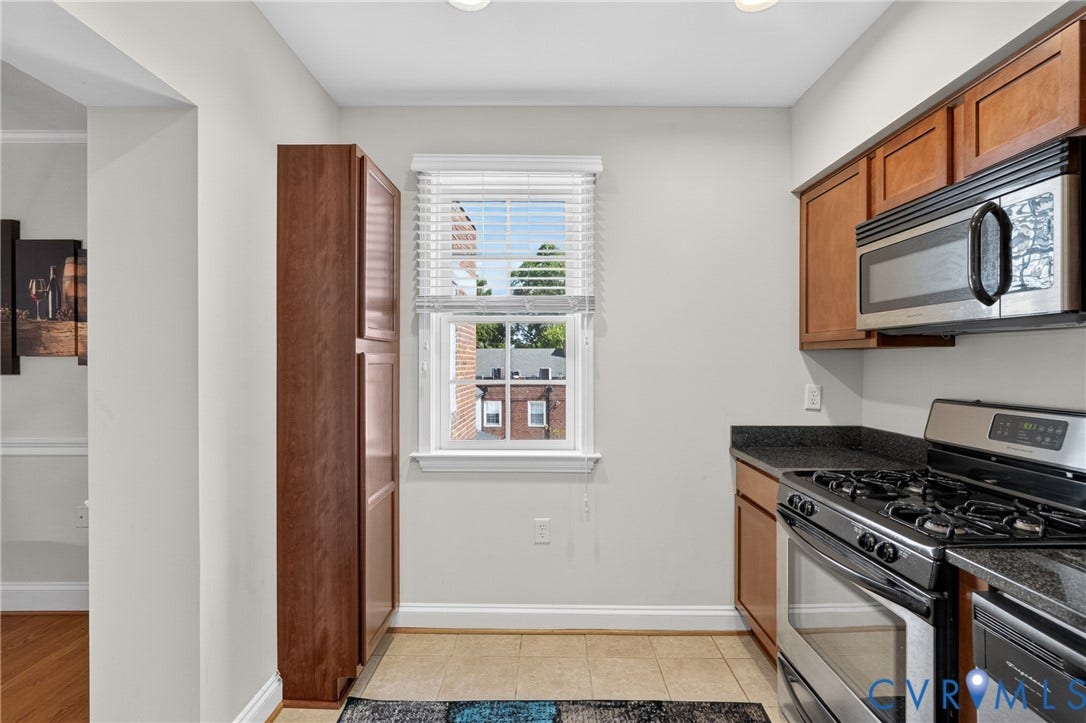 Wood-finish cabinetry, stainless steel appliances, dark stone-finish countertops, and tiled flooring