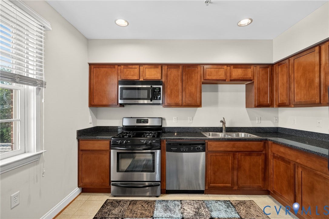 Kitchen featuring wood cabinetry, stainless steel appliances, dark countertops, and recessed lighting