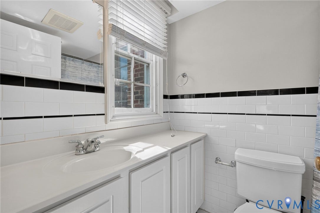 White subway tile walls with black accent banding, white vanity with integrated sink, chrome faucet, and white paneled cabinetry