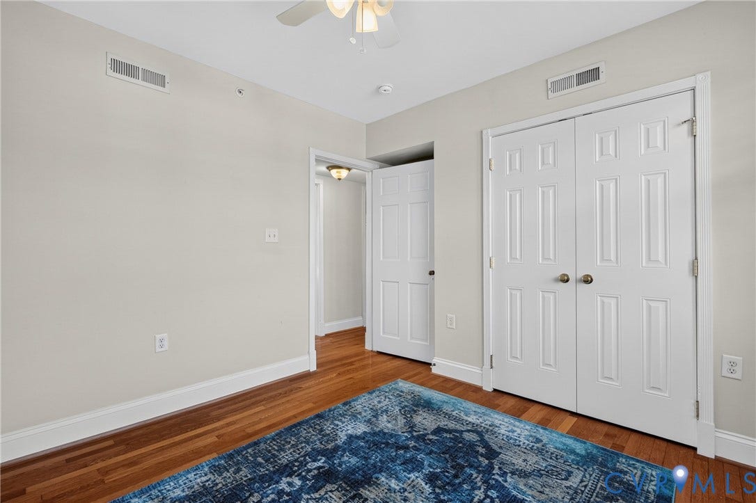 Hardwood flooring throughout, white six-panel bifold closet doors, light-toned wall paint, and a ceiling fan with integrated lighting