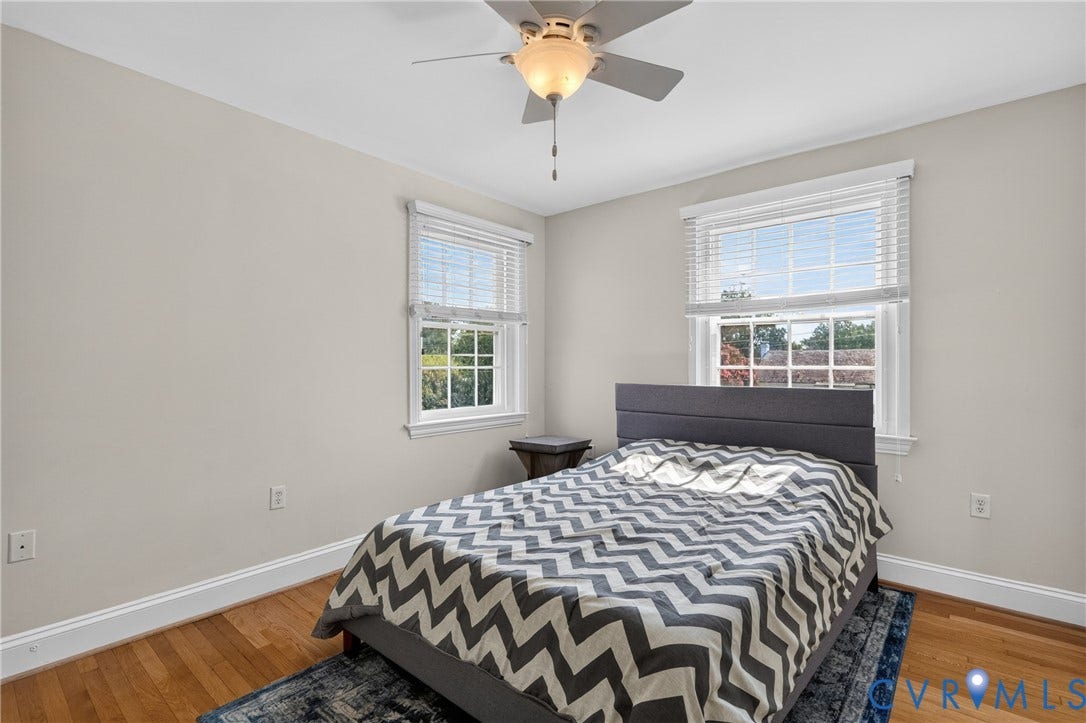 Hardwood flooring, light neutral wall paint, two windows with blinds, and a ceiling fan with integrated lighting