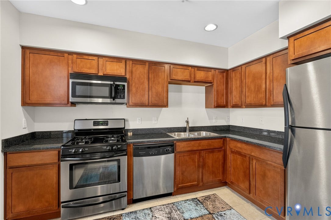 Kitchen featuring stainless steel appliances, wood-finish cabinetry, dark countertops, and a dual basin sink