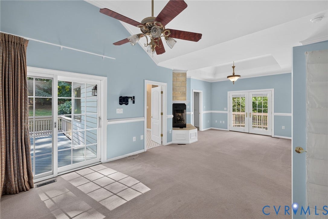 365 Hamlet Road, Manakin Sabot, VA 23103 Vaulted ceiling with ceiling fan, corner fireplace with stone surround, tray ceiling with chandelier, and dual French doors opening to an exterior deck