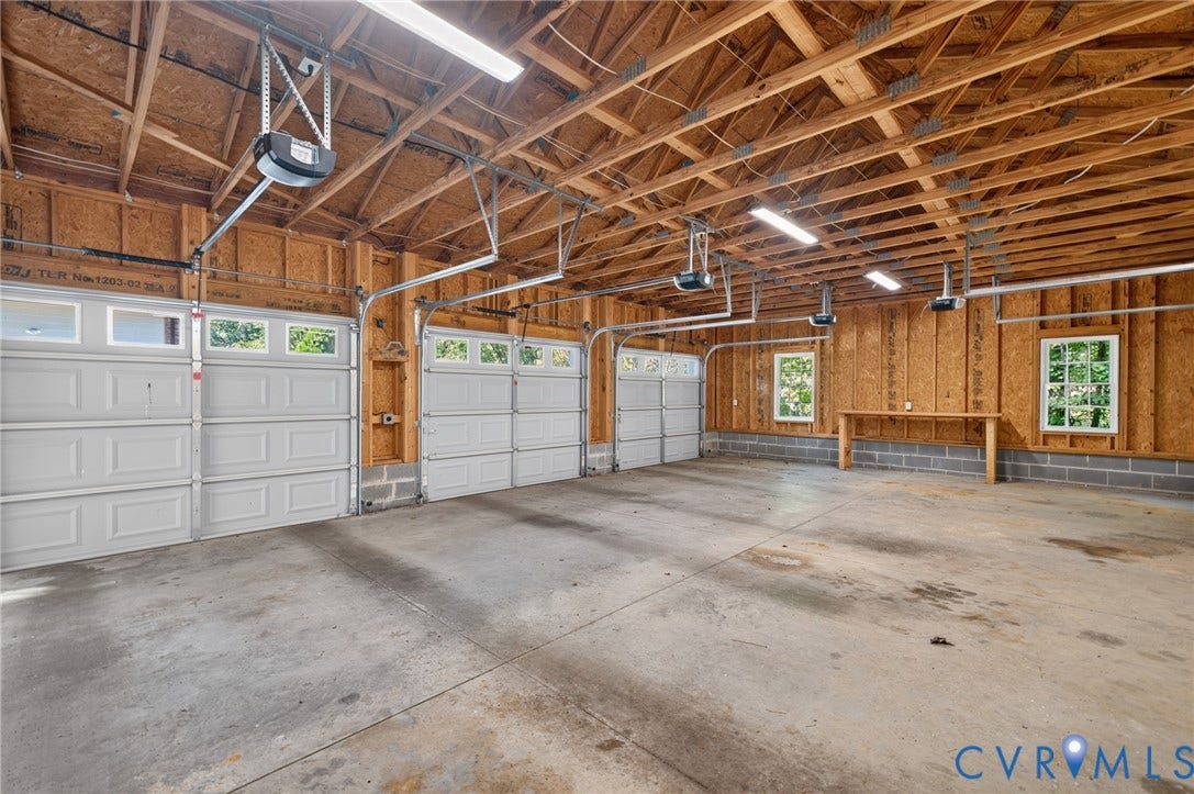 365 Hamlet Road, Manakin Sabot, VA 23103 Three overhead garage doors with frosted windows, exposed wood beam ceiling, concrete flooring, and built-in workbench