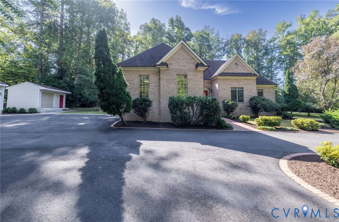 365 Hamlet Road, Manakin Sabot, VA 23103 Brick exterior with a gabled roofline, mature trees, landscaped shrubbery, a paved driveway, and a detached outbuilding