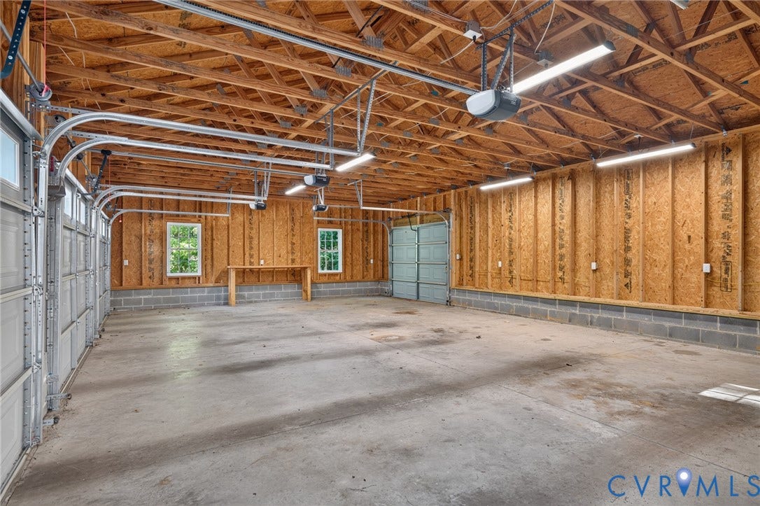 365 Hamlet Road, Manakin Sabot, VA 23103 Spacious garage featuring concrete flooring, exposed wood beam ceiling, multiple fluorescent light fixtures, two windows, and a built-in workbench
