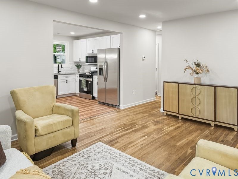 Hardwood flooring throughout, recessed lighting, and a kitchen featuring white cabinetry, stainless steel appliances, and a tile backsplash