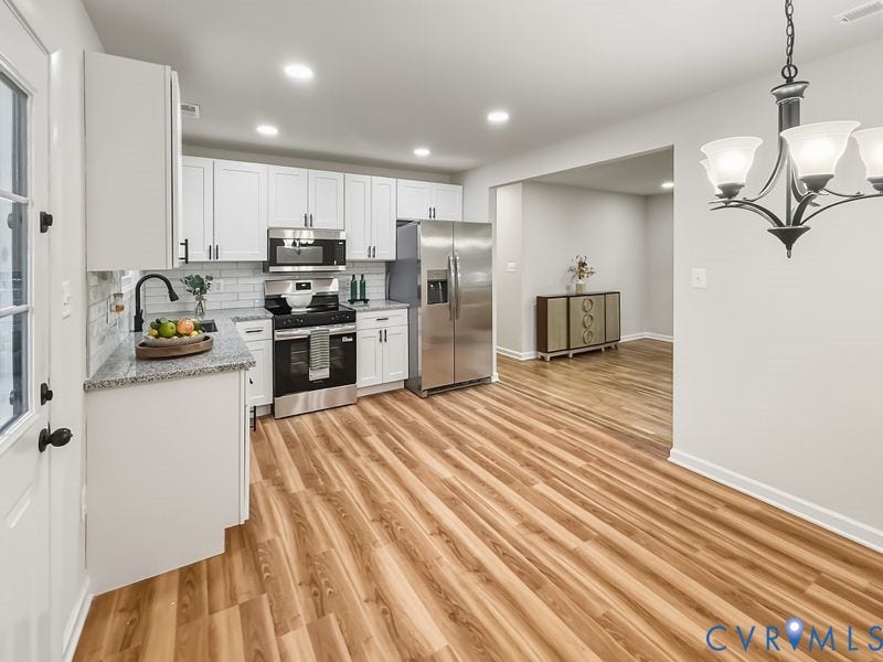 Modern kitchen featuring white cabinetry, stainless steel appliances, granite countertops, and wood-finish flooring