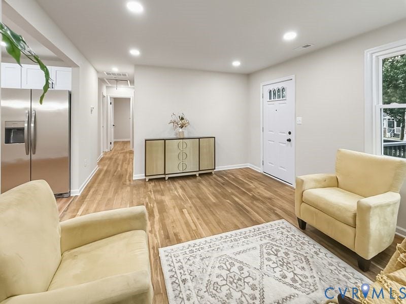 Wood-finish flooring throughout, recessed lighting, stainless steel refrigerator, white cabinetry, and a white entry door with decorative glass inserts