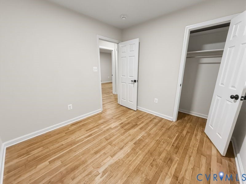 Wood-finish flooring, white paneled doors with black hardware, and an open closet with shelving and hanging rods