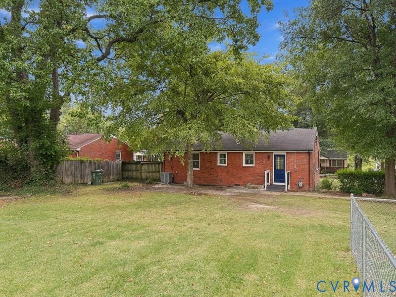 Expansive grassy yard with mature trees, brick exterior, blue entry door, and perimeter fencing
