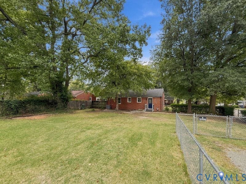 Expansive green lawn with mature trees and partial chain link fencing