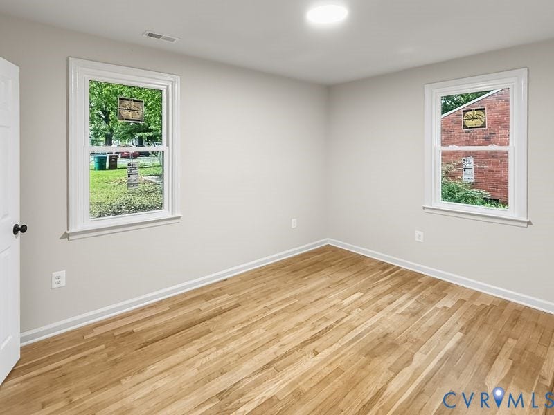 Hardwood flooring, light gray wall paint, white trim, and two windows