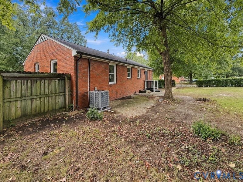 Brick exterior with white-framed windows, a prominent tree, and a wooden fence