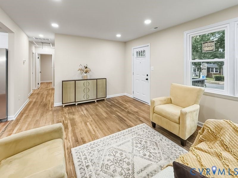 Hardwood flooring throughout, recessed lighting, white paneled entry door with decorative glass, and multiple windows