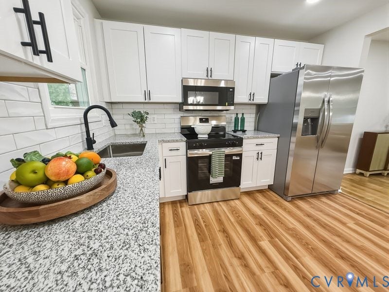 Kitchen featuring white shaker cabinetry, stainless steel appliances, speckled countertops, subway tile backsplash, and wood-finish flooring
