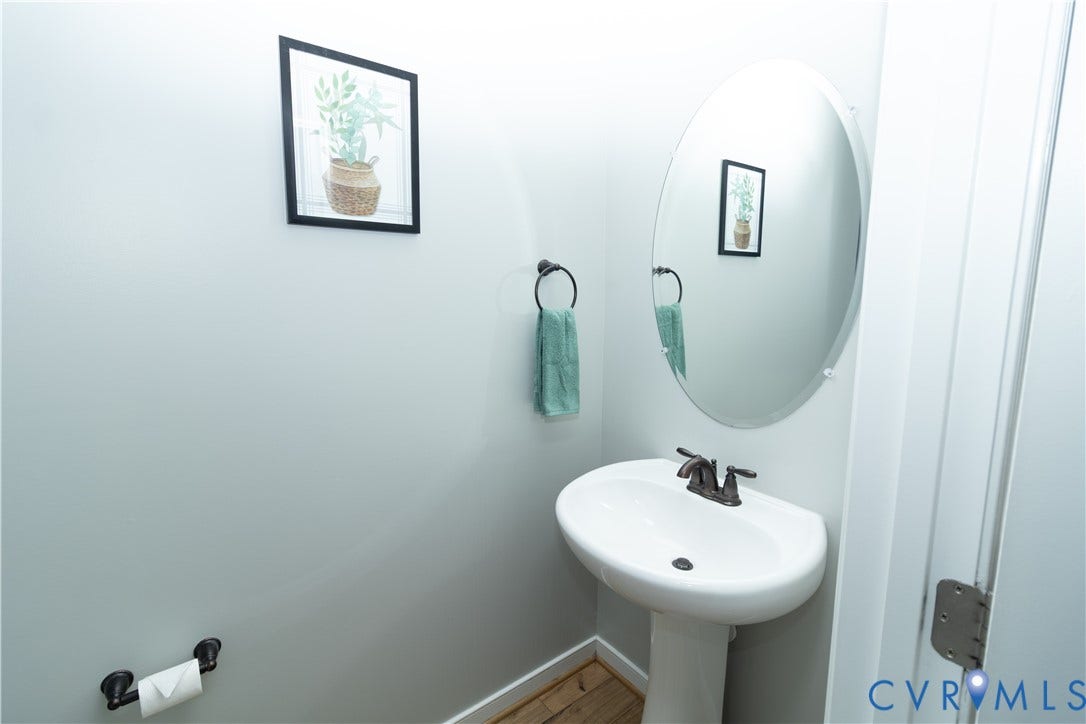 White pedestal sink with a bronze-finish faucet, oval mirror, and wood-finish flooring