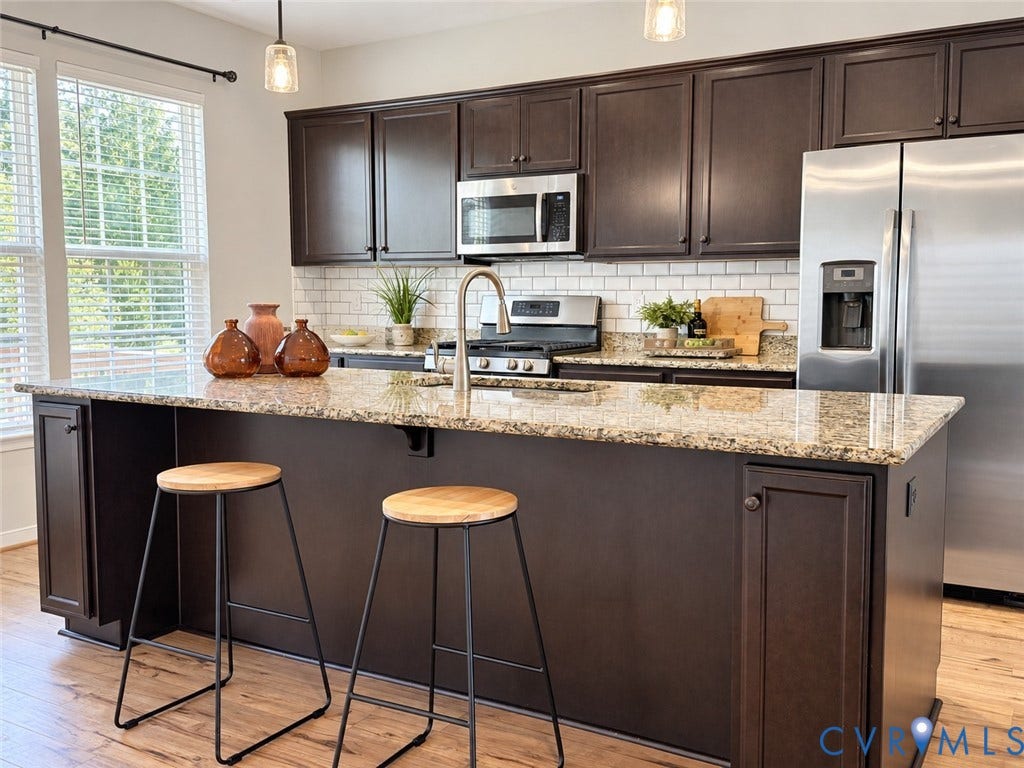 Kitchen featuring a central island with a granite countertop, dark wood-finish cabinetry, stainless steel appliances, and a subway tile backsplash