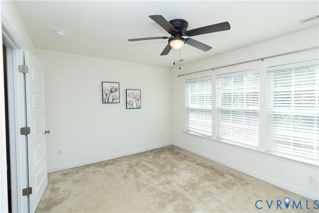 Wall-to-wall carpeting with a ceiling fan light fixture, three large windows, and white paneled door