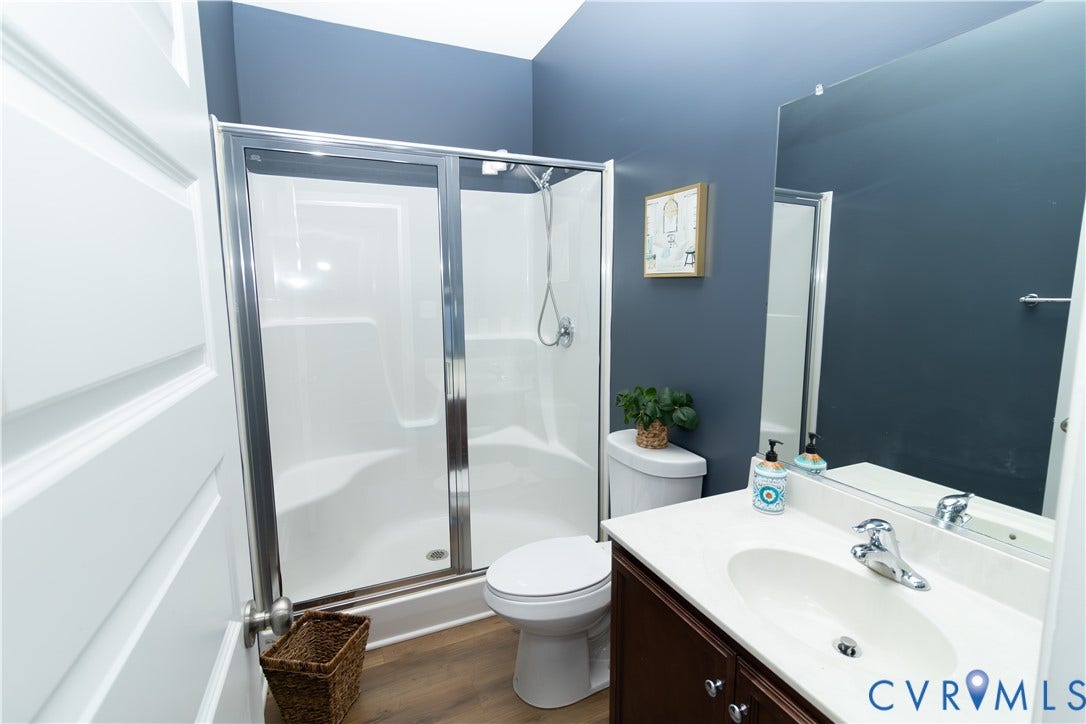 Shower with sliding glass enclosure, wood-finish flooring, single vanity with integrated sink, and wall-mounted mirror