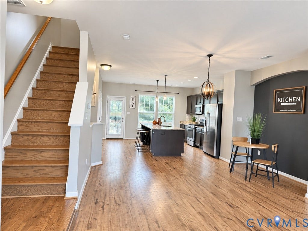 Wood-finish flooring throughout, kitchen island with seating, stainless steel appliances, dark wood cabinetry, and a prominent staircase with wood treads