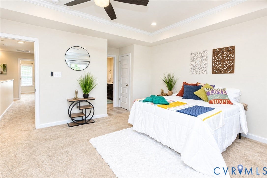 Tray ceiling with recessed lighting, ceiling fan, neutral carpet flooring, and a doorway leading to an adjoining space