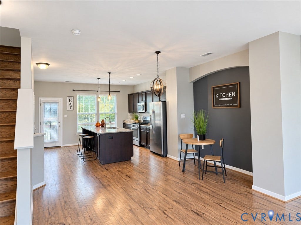 Open-concept living area featuring wood-finish flooring, a kitchen island with seating, stainless steel appliances, and a staircase with wood treads