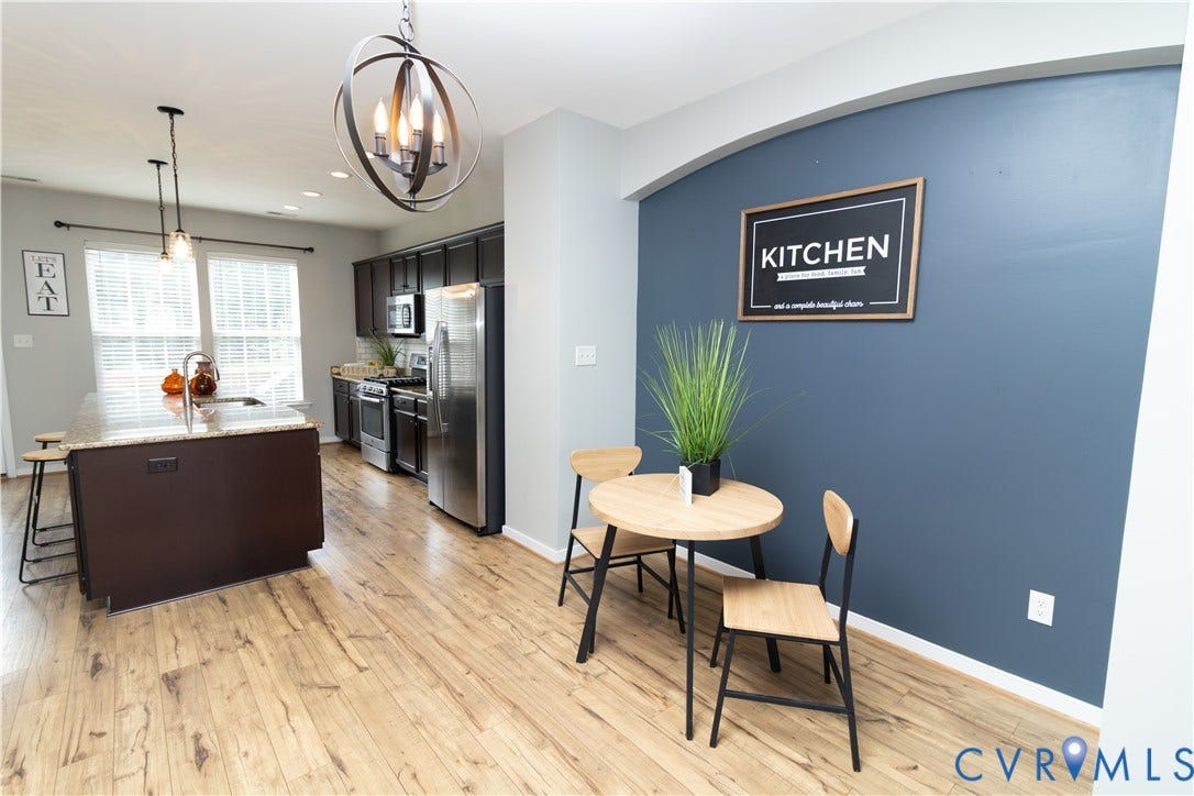 Kitchen featuring wood-finish flooring, dark cabinetry, stainless steel appliances, and a central island with a granite-style countertop