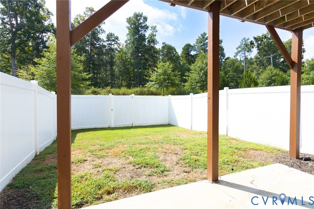 Fenced backyard featuring a grassy area, concrete patio, and mature trees