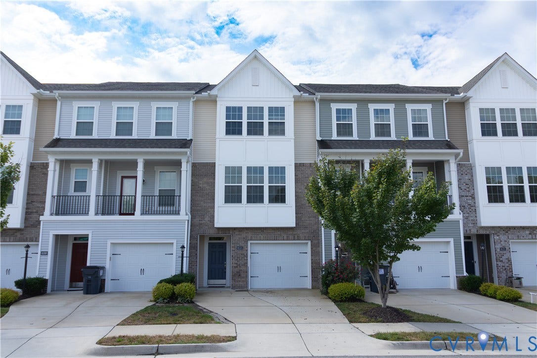Multi-level townhome with an attached garage, featuring a front balcony with black railings, and a combination of siding and brick exterior finishes