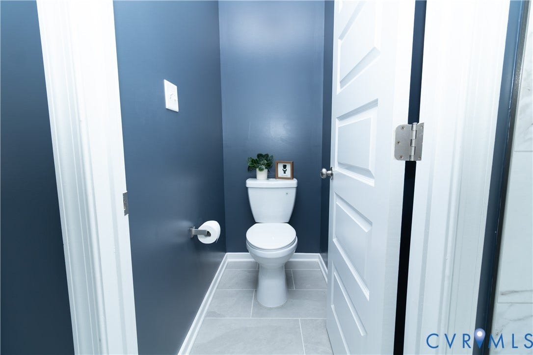 Recessed toilet with a white ceramic fixture, a wall-mounted toilet paper holder, and light gray tile flooring