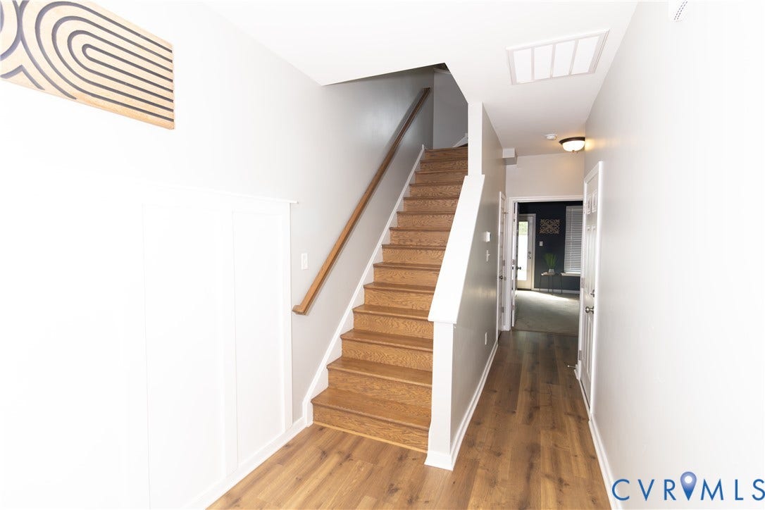 Wood-finish flooring, white wall paneling, natural wood handrail, and flush mount lighting