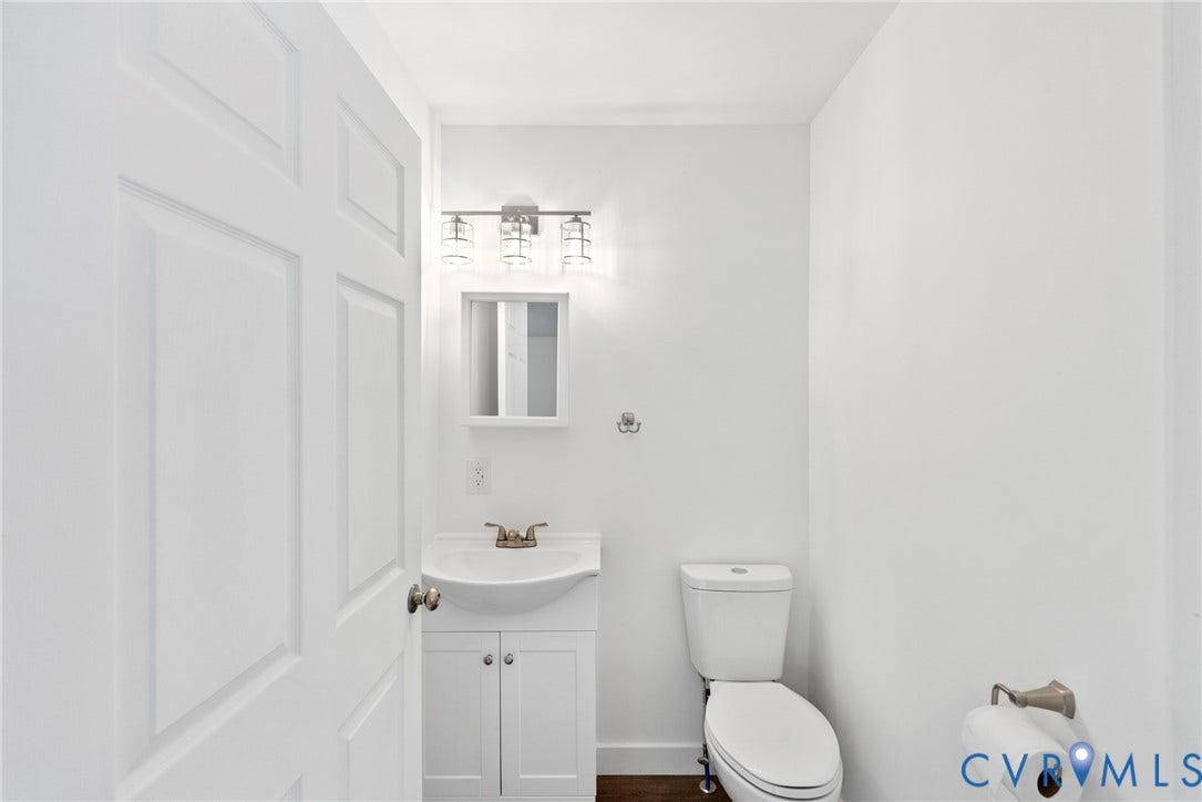7621 Amelia Springs Road, Amelia, VA 23083 White paneled door, wall-mounted vanity light, framed mirror, white toilet, and wood-finish flooring