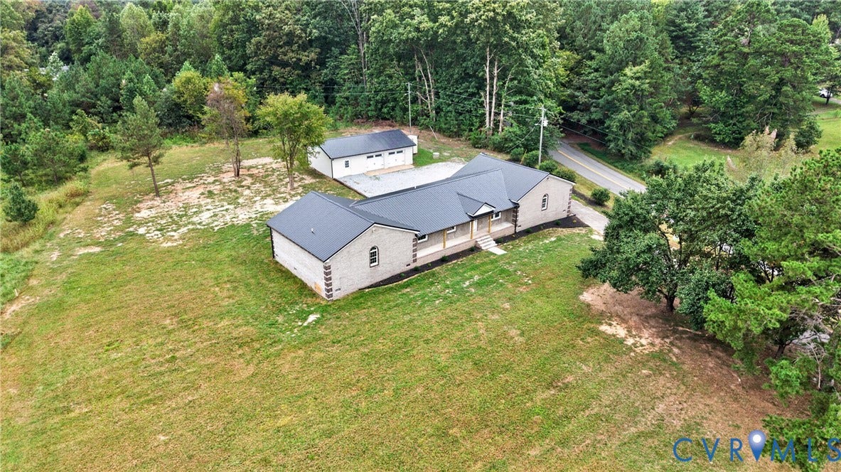 7621 Amelia Springs Road, Amelia, VA 23083 Light-colored brick exterior, dark gray metal roof, covered front porch, detached garage building, and surrounding mature trees