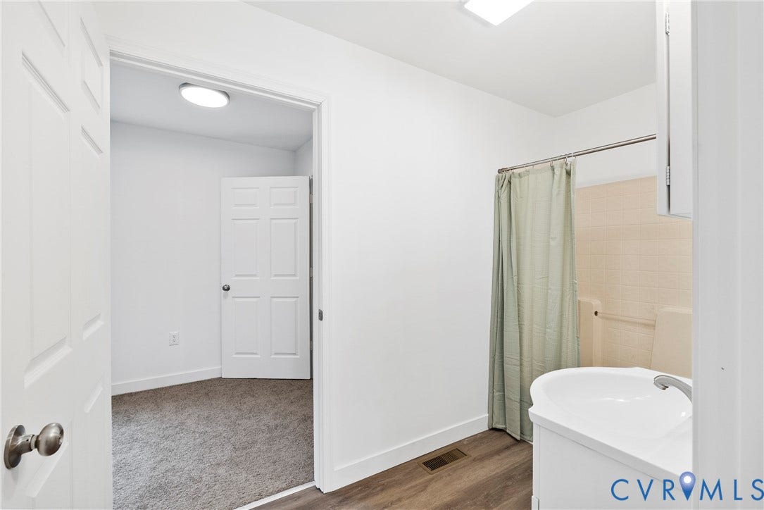 7621 Amelia Springs Road, Amelia, VA 23083 Vanity with integrated sink, wood-finish flooring, white paneled doors, and tiled shower area