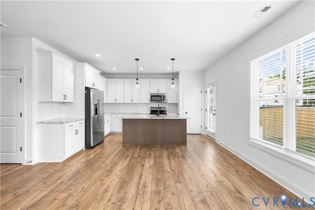 Kitchen featuring white cabinetry, stainless steel appliances, a center island, and wood-finish flooring