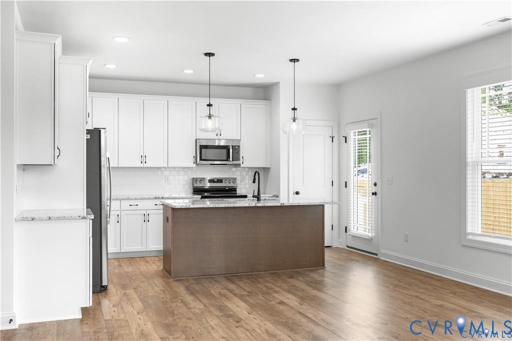 Bright kitchen featuring white cabinetry, stainless steel appliances, wood-finish flooring, and a central island with pendant lighting