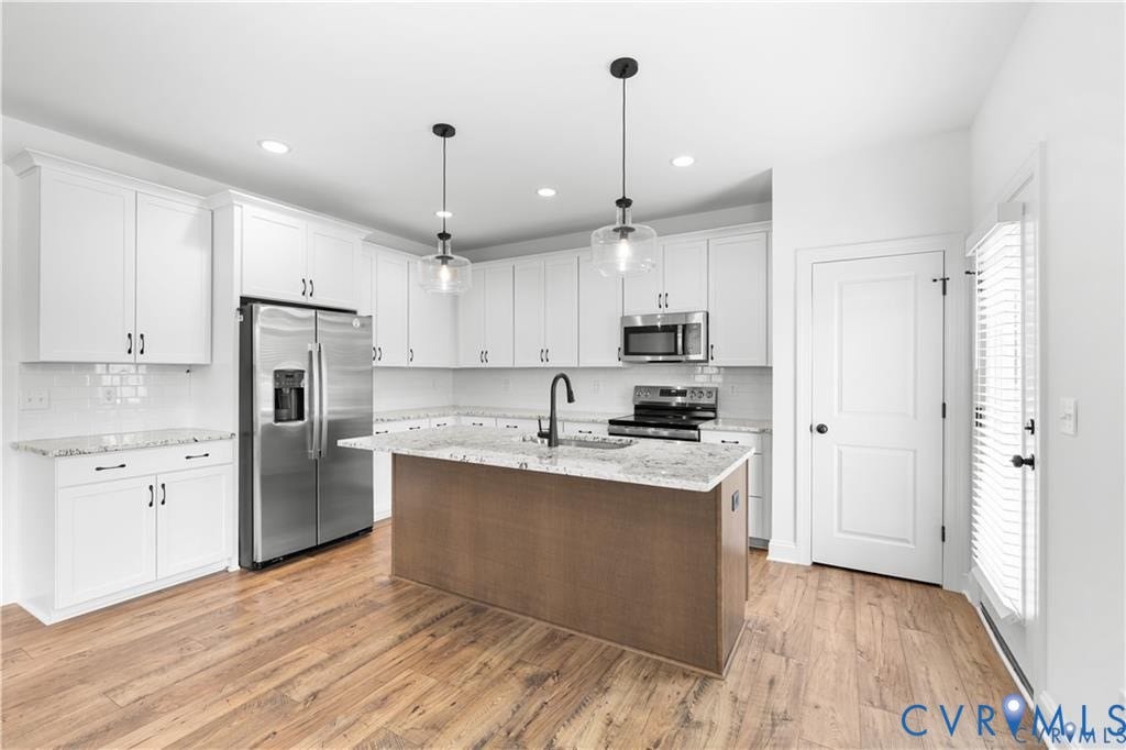 White cabinetry, stainless steel appliances, granite countertops, wood-finish flooring, and a kitchen island with pendant lighting