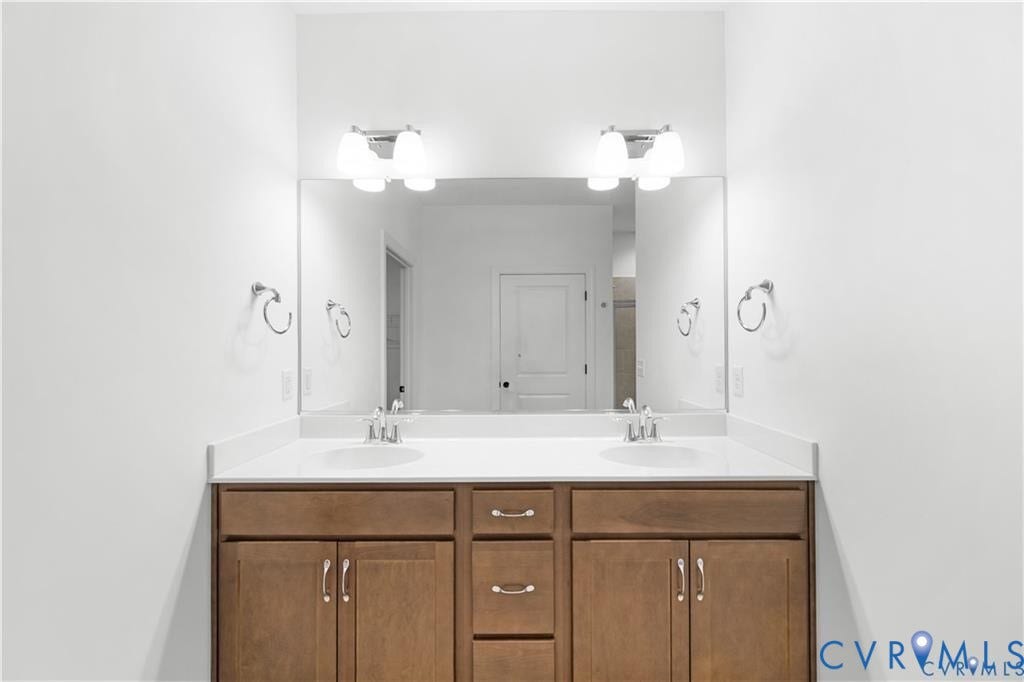 Dual vanity with wood-finish cabinetry and white countertop, featuring two integrated sinks and chrome fixtures