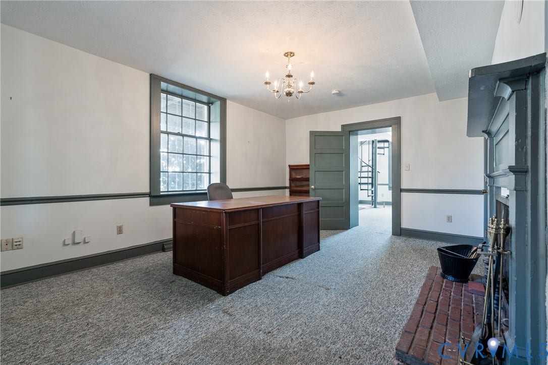 13085 W James Anderson Highway, Buckingham, VA 23921 Carpeted room featuring a chandelier, a window with dark trim, a decorative fireplace with a brick hearth, and a doorway leading to a spiral staircase