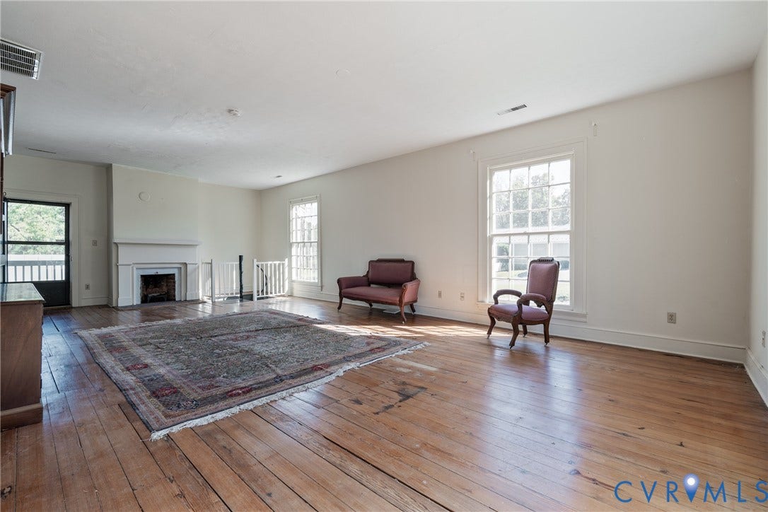 13085 W James Anderson Highway, Buckingham, VA 23921 Spacious room featuring wide plank wood flooring, a decorative fireplace with a mantel, multiple windows, and a door with a screen
