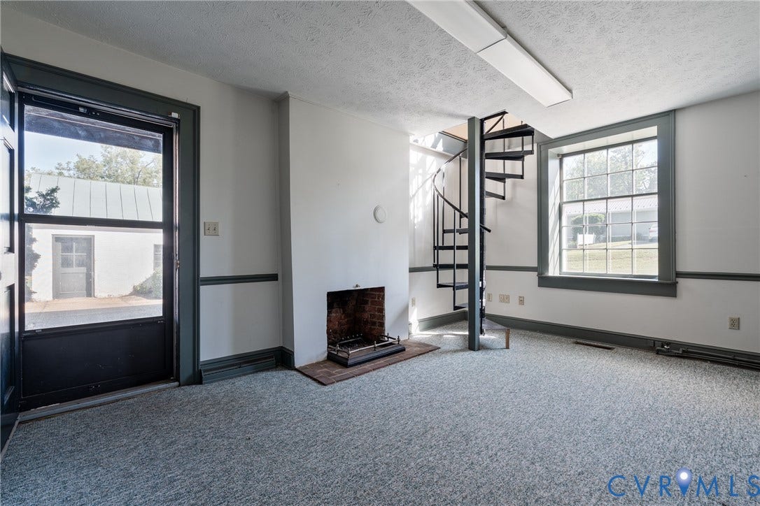 13085 W James Anderson Highway, Buckingham, VA 23921 Brick fireplace with hearth, spiral staircase, large multi-pane window, and wall-to-wall carpeting