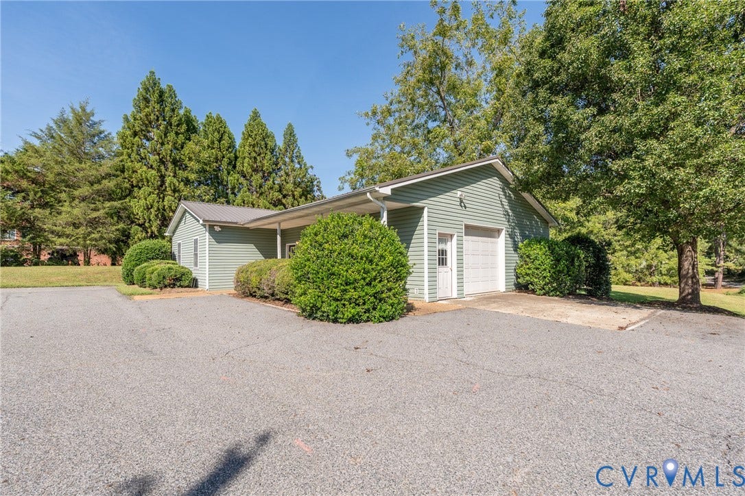 13085 W James Anderson Highway, Buckingham, VA 23921 Exterior featuring a light green siding, covered entry, attached garage with a white door, and mature landscaping