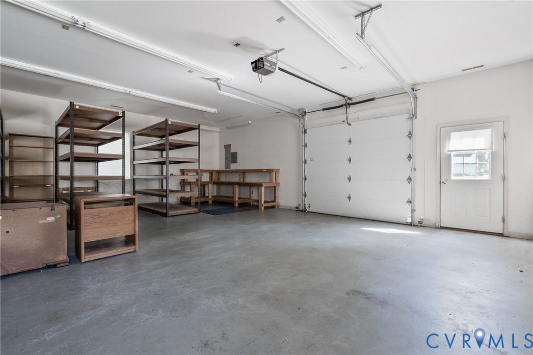13085 W James Anderson Highway, Buckingham, VA 23921 Spacious garage with a roll-up door, side-entry door with glass pane, fluorescent lighting, and concrete flooring