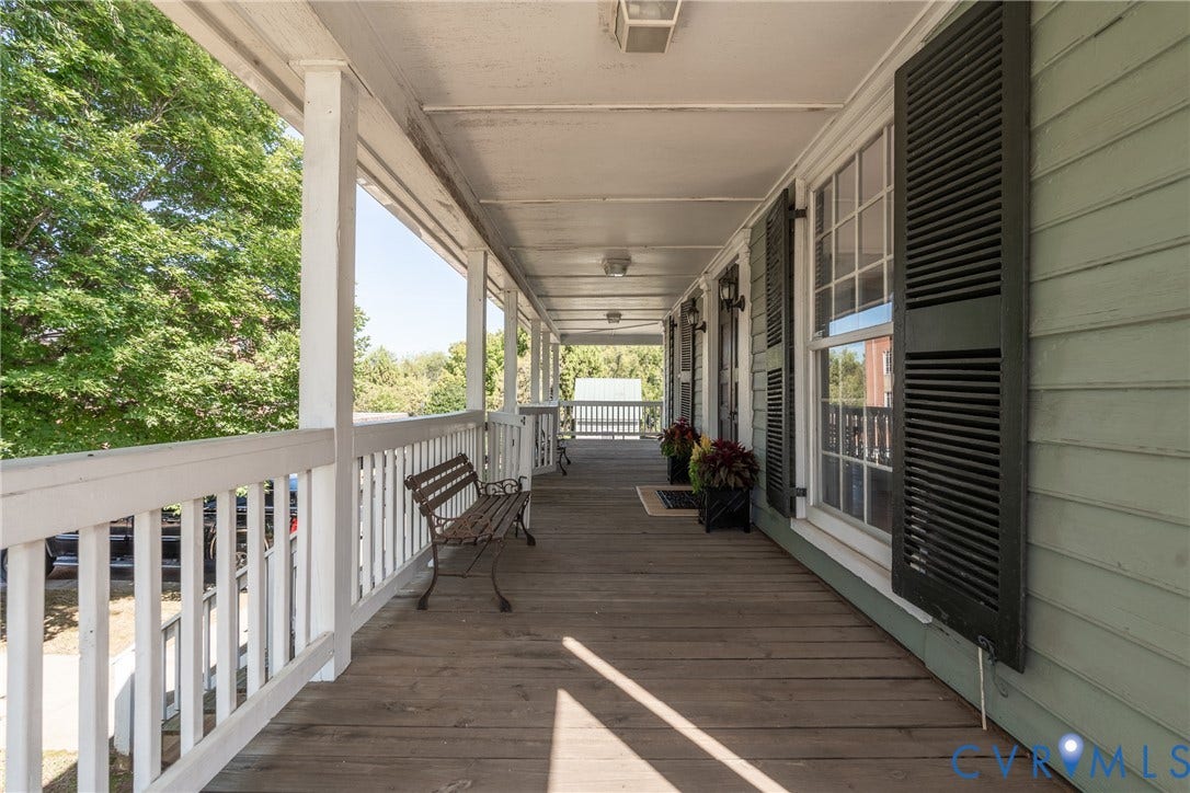 13085 W James Anderson Highway, Buckingham, VA 23921 Expansive covered porch featuring a painted wood railing, exposed wood-finish flooring, and multiple window units with louvered shutters