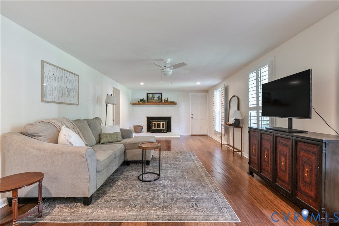 4327 Wakefield Road, Stratford Hills, Richmond, VA 23235 Spacious living area featuring wood-finish flooring, a white brick fireplace with a wood mantle, and white plantation shutters on the windows