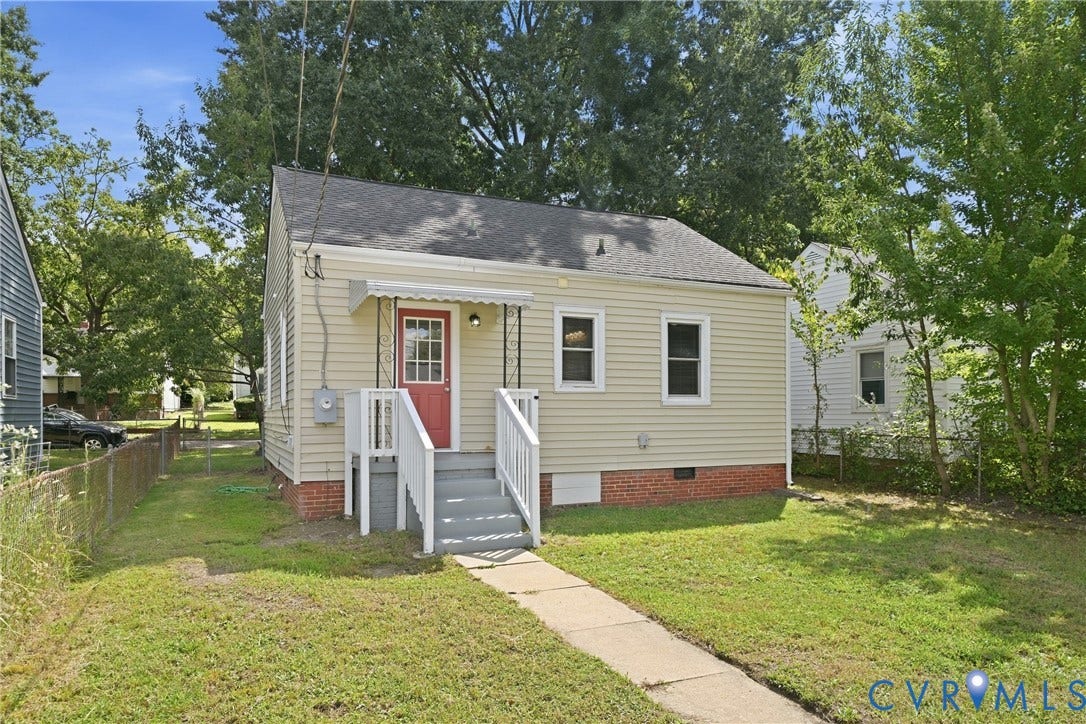 1718 Rogers, Richmond, VA 23223 Beige vinyl siding with a red paneled entry door, white porch railing, a concrete walkway, and a partial chain-link fence