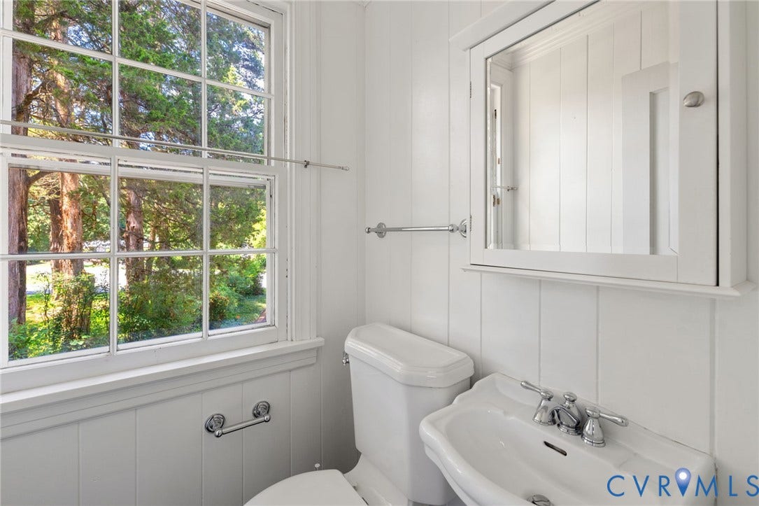 White paneled walls, white sash window, wall-mounted sink, medicine cabinet with mirror, and polished chrome fixtures