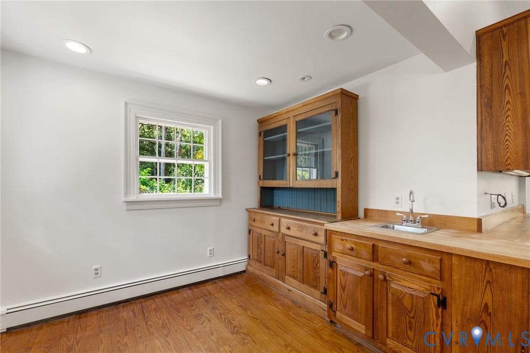 Wood-finish flooring with a white trim, featuring a built-in wood cabinet with glass doors and a sink with a metal faucet